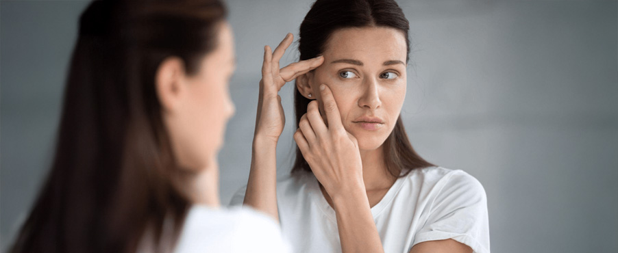 Ciemnowłosa kobieta przegląda się w lustrze i ocenia stan swojej skóry